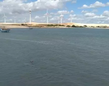 Rio com geradores eólicos nas dunas ao fundo